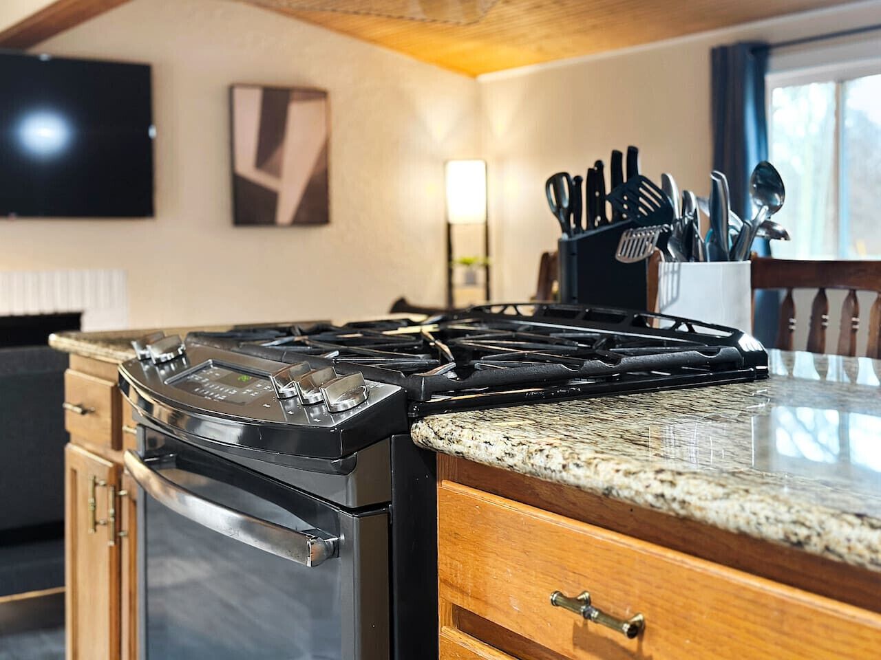 A kitchen with a gas stove, granite countertop, wooden cabinets, and a knife holder.