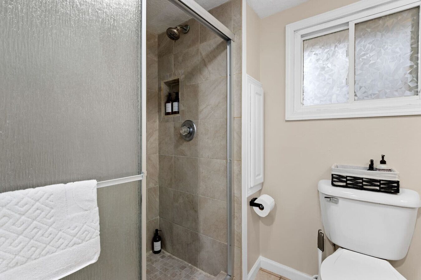 Un baño con ducha, inodoro y ventana con vidrio esmerilado.