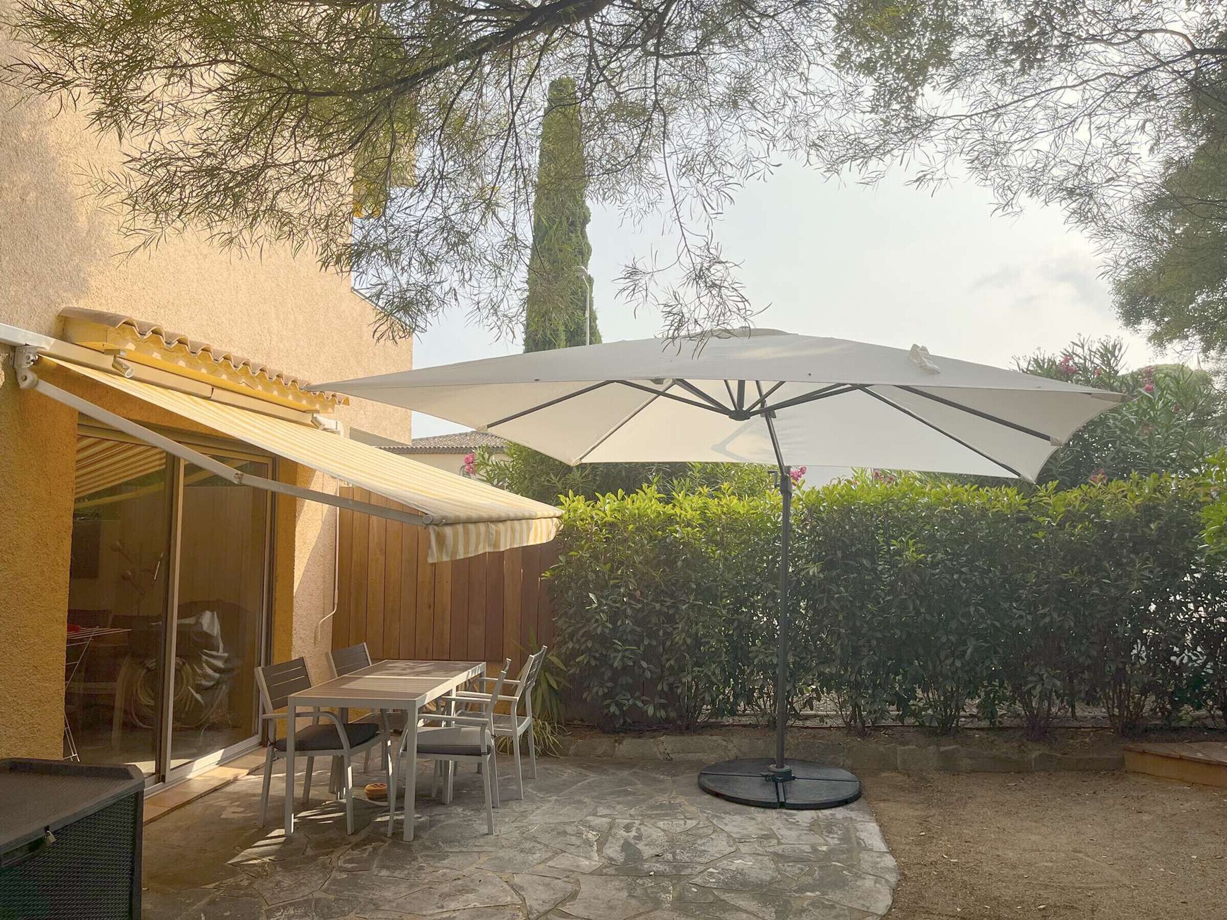 An outdoor patio with a table and chairs, a large umbrella, and a stone floor.