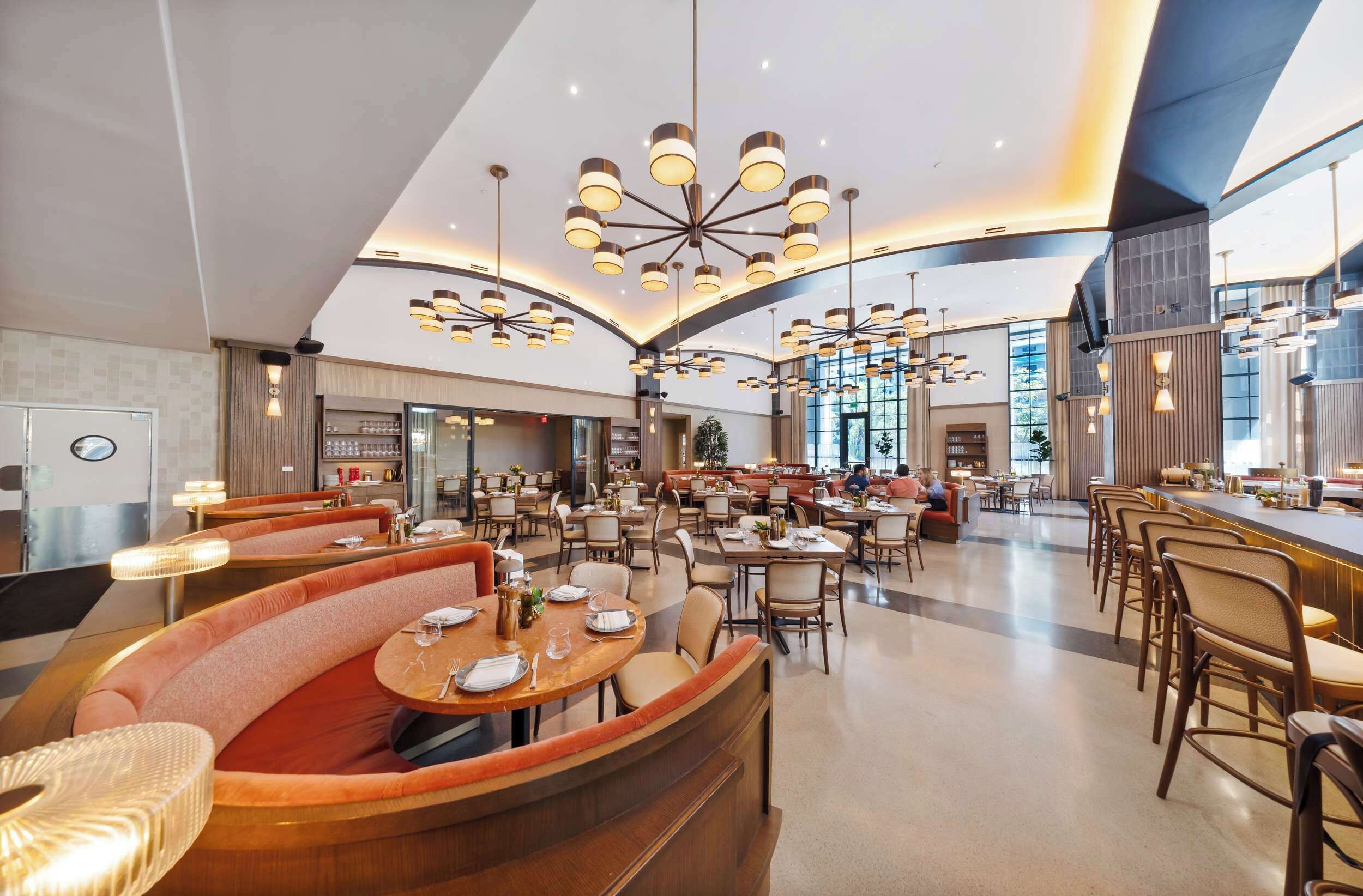 Un hall d’hôtel spacieux, doté de plusieurs espaces de détente, notamment un coin salon incurvé et plusieurs tables et chaises.