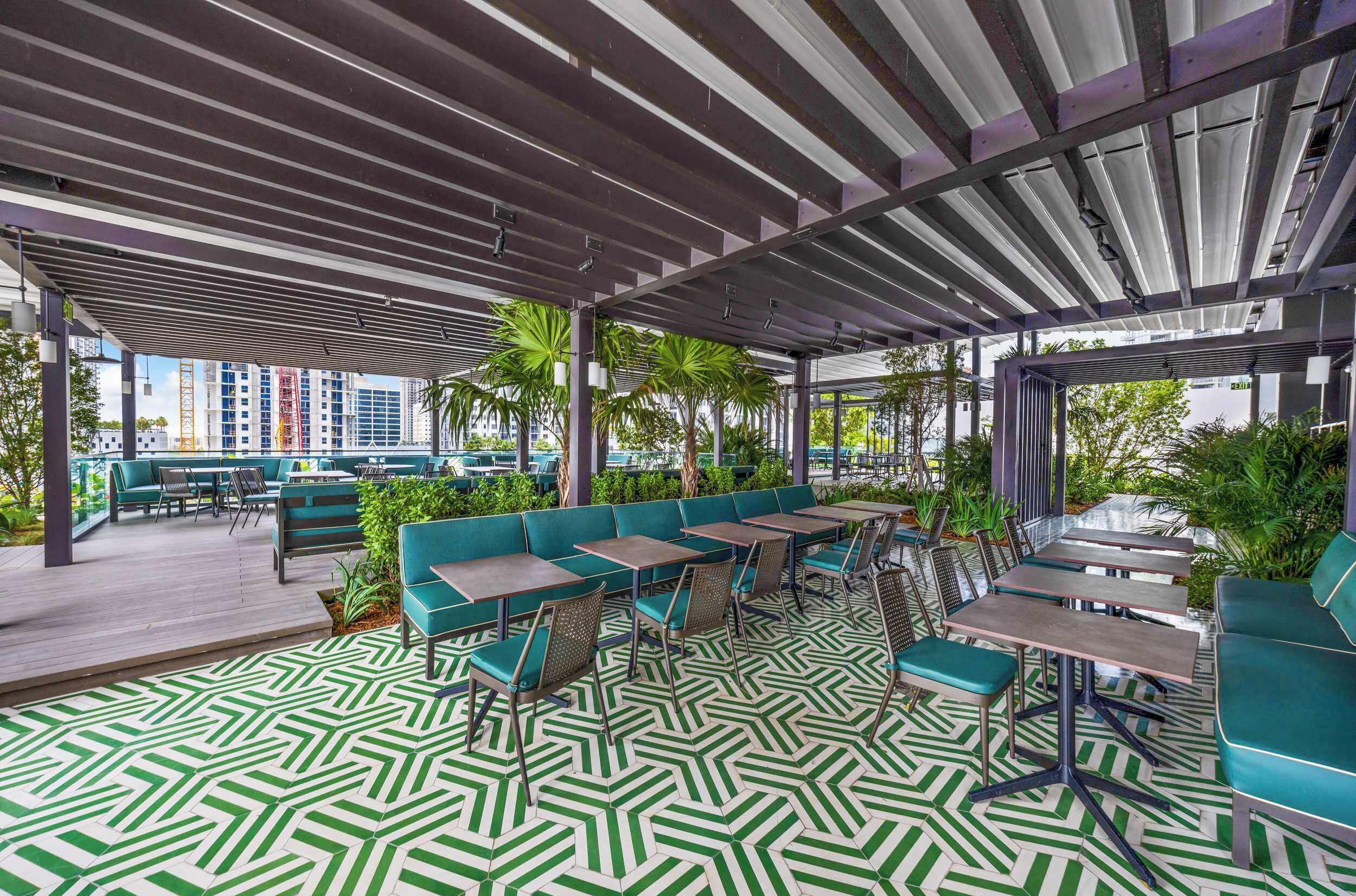An outdoor seating area with green and white patterned flooring, green cushioned seating, and tables.