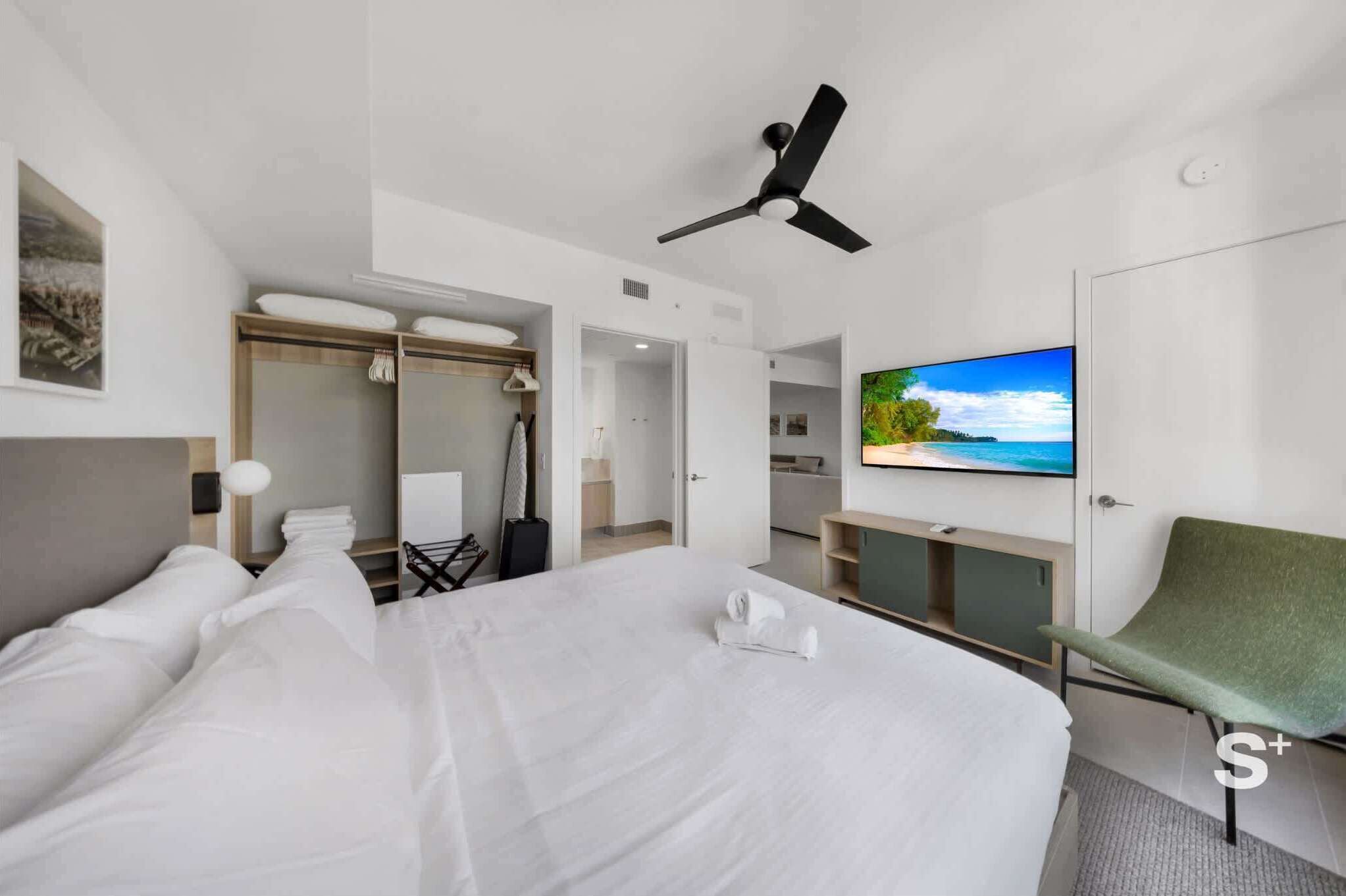 Une chambre d’hôtel avec un grand lit, une télévision, un ventilateur de plafond, un fauteuil vert et une vue sur la mer.
