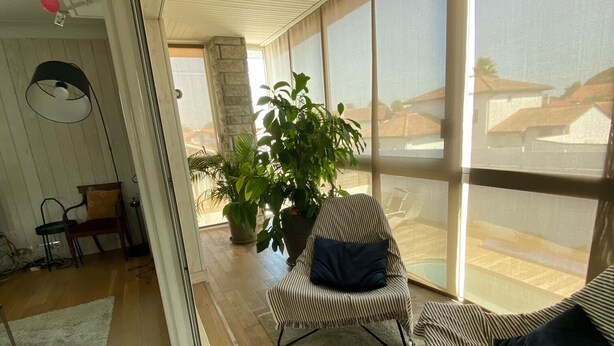 Une pièce spacieuse dotée d’une grande porte-fenêtre coulissante donnant sur un balcon, d’un fauteuil à rayures, d’un canapé et d’une plante en pot.