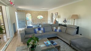 Un salon moderne avec un canapé d’angle gris, une table basse en verre et un tapis moelleux.