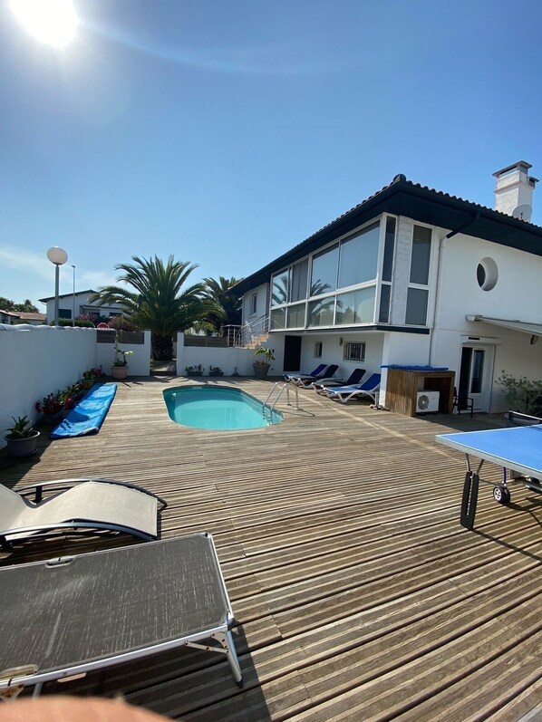 Una casa moderna con piscina, terraza de madera y sillones de descanso.