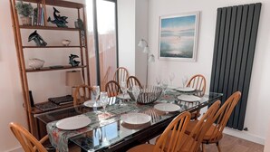 Un coin repas avec une table en verre, des chaises en bois et une bibliothèque agrémentée d’objets décoratifs.