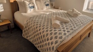 Un lit bien fait, recouvert d’une couvre-lit à motifs, avec deux oreillers décorés de motifs de crabes et deux serviettes enroulées posées sur le lit.