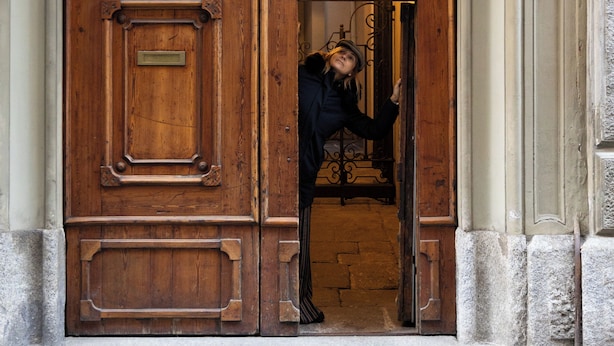 Une grande porte à double battant en bois, ornée d’une plaque en laiton et surmontée du chiffre « 24 », ainsi qu’un mur de pierre agrémenté d’éléments décoratifs sur la droite.