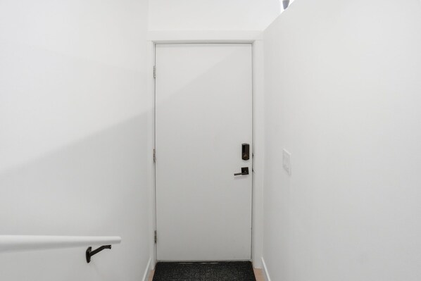 A narrow hallway with a white door, a black doorknob, and a black doormat at the entrance.
