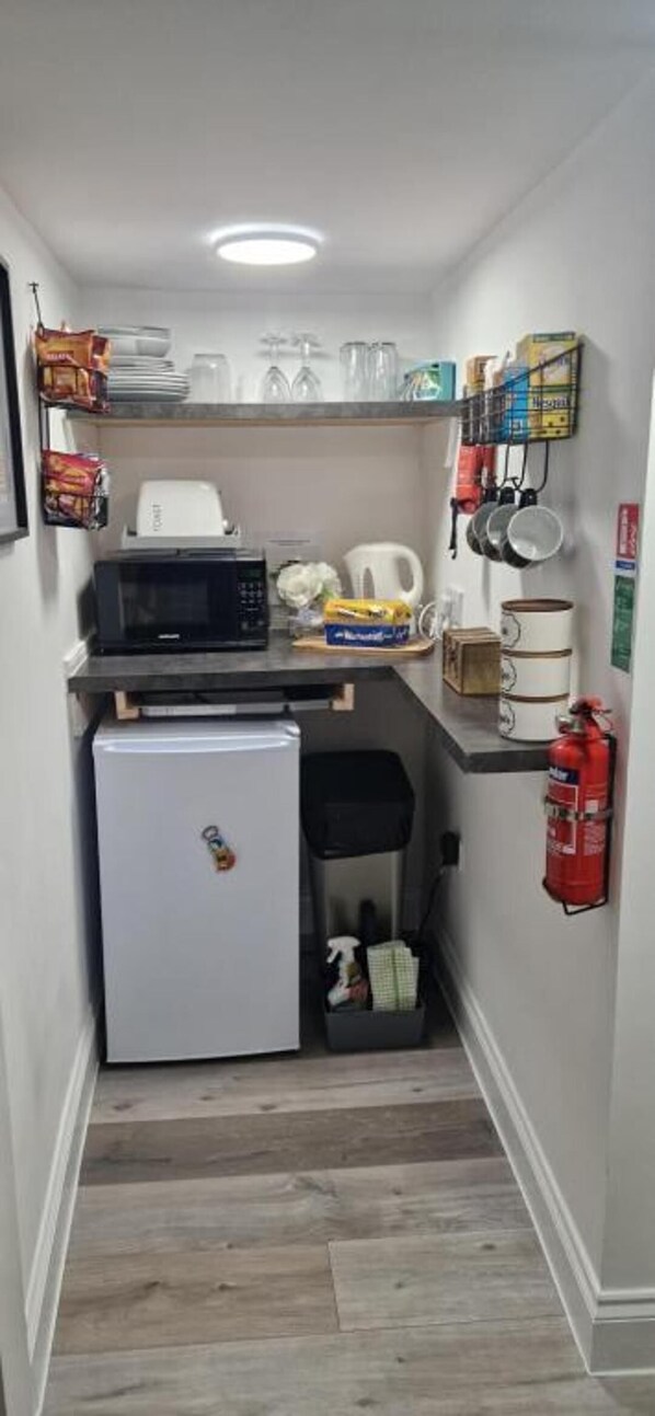 A compact kitchenette with a microwave, refrigerator, and a small trash bin. - High Street Apartment Getaway in Inverurie (Inverurie)