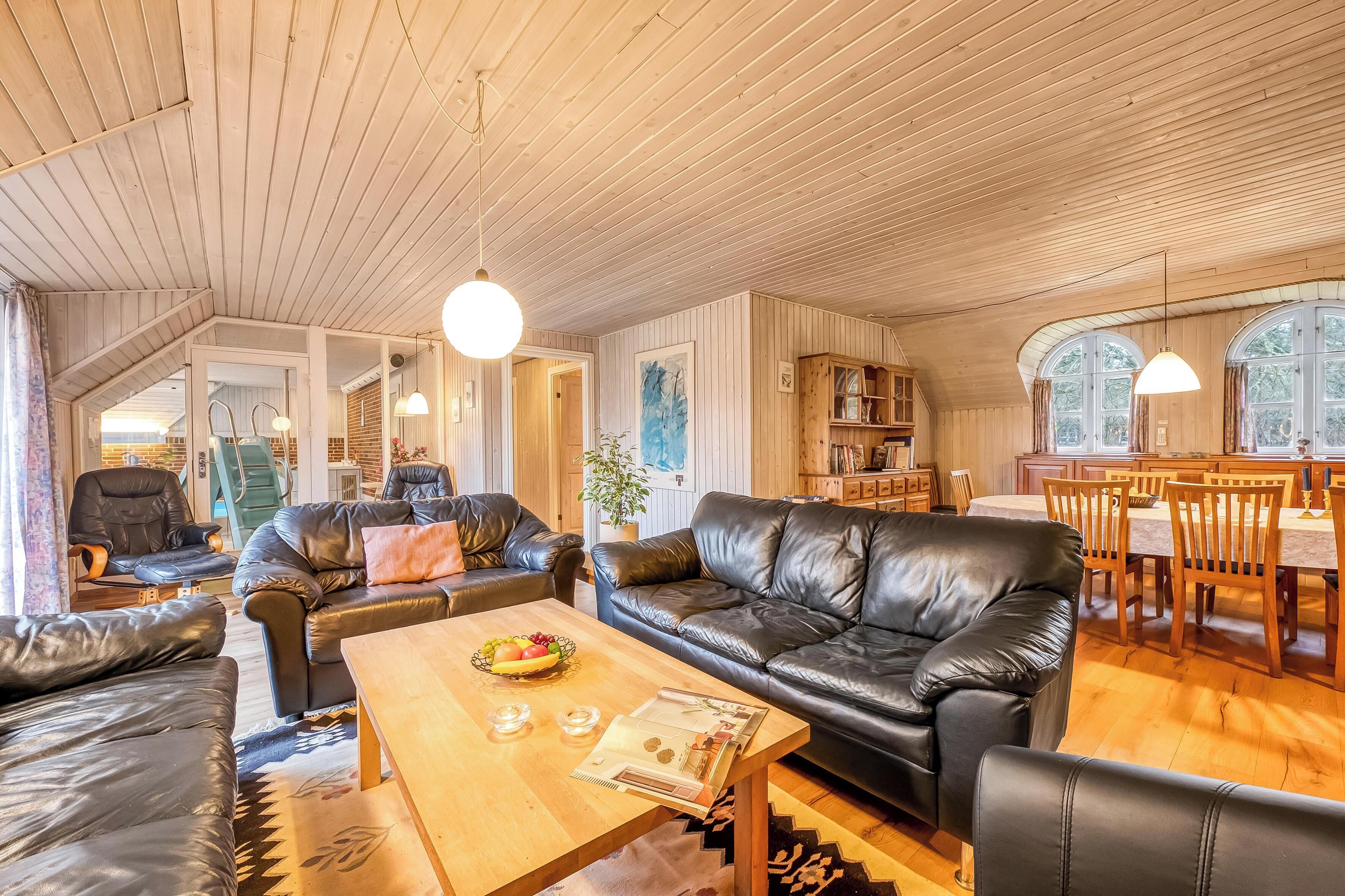 A spacious living room with a wooden ceiling, leather sofas, a wooden coffee table, and a dining area with a wooden table and chairs.