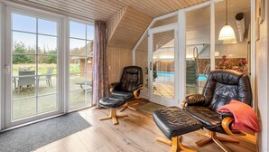 A spacious room with large sliding glass doors leading to an outdoor area, featuring two leather recliners and a dining table.