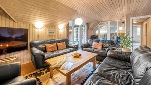 A spacious living room with leather sofas, a wooden coffee table, and a large flat-screen TV.