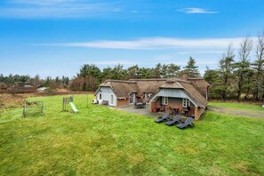 A thatched-roof house with a patio area, a play structure, and a lawn. - Large holiday home with pool, spa and sauna, 1500 meters from the North Sea. (Ulfborg)