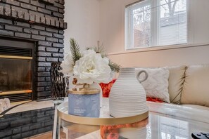 A living room with a fireplace, a sofa, a coffee table with decorative items, and a window with blinds. - Wesley -Large 5bdrm 3 baths home, minutes to WEM! (Edmonton)