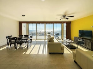 Relax in this stylish living area with a balcony offering a city view, featuring a dining table, sofa, and TV.