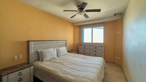A bedroom with a bed, nightstands, a dresser, a ceiling fan, and a window.