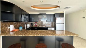 A modern kitchen with dark cabinets, a granite countertop, a central island with stools, and stainless steel appliances.