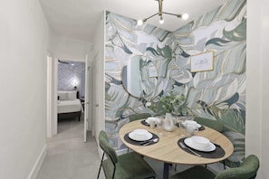 Un coin repas avec une table ronde, des chaises recouvertes d’un tissu vert et un mur orné d’un motif de feuilles.