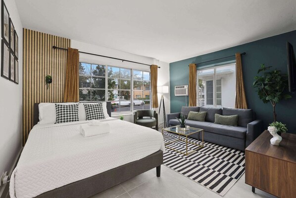 Ein modernes Hotelzimmer mit einem großen Bett, einer Couch, einem Couchtisch und Blick auf die Straße.