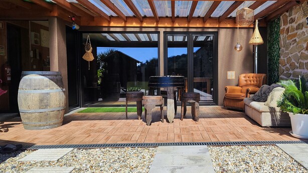 A covered outdoor patio with a wooden table and chairs, a stone barrel, and a seating area with a sofa and potted plants. - La Cigarrita Guest House - Douro Valley (Peso da Régua)