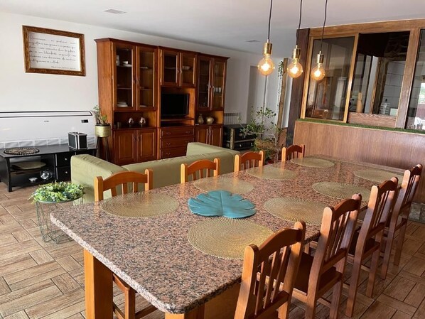 A dining area with a granite table, wooden chairs, and a glass-top dining table. There is a wooden cabinet with glass doors and a television on a stand. - La Cigarrita Guest House - Douro Valley (Peso da Régua)