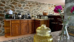 A kitchen with a stone wall, wooden cabinets, a granite countertop, a coffee maker, a toaster, a kettle, and a vase with flowers. - La Cigarrita Guest House - Douro Valley (Peso da Régua)