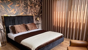 A modern bedroom with a dark headboard, a large bed with brown bedding, a wooden floor, and a window with vertical blinds. - La Cigarrita Guest House - Douro Valley (Peso da Régua)