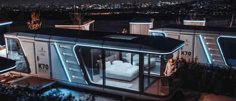 A modern, glass-walled bedroom with a city view, a private outdoor area, and a snow-covered ground.