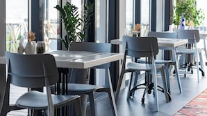 Et moderne spiseområde med store vinduer, borde, stole og et mønstret tæppe.