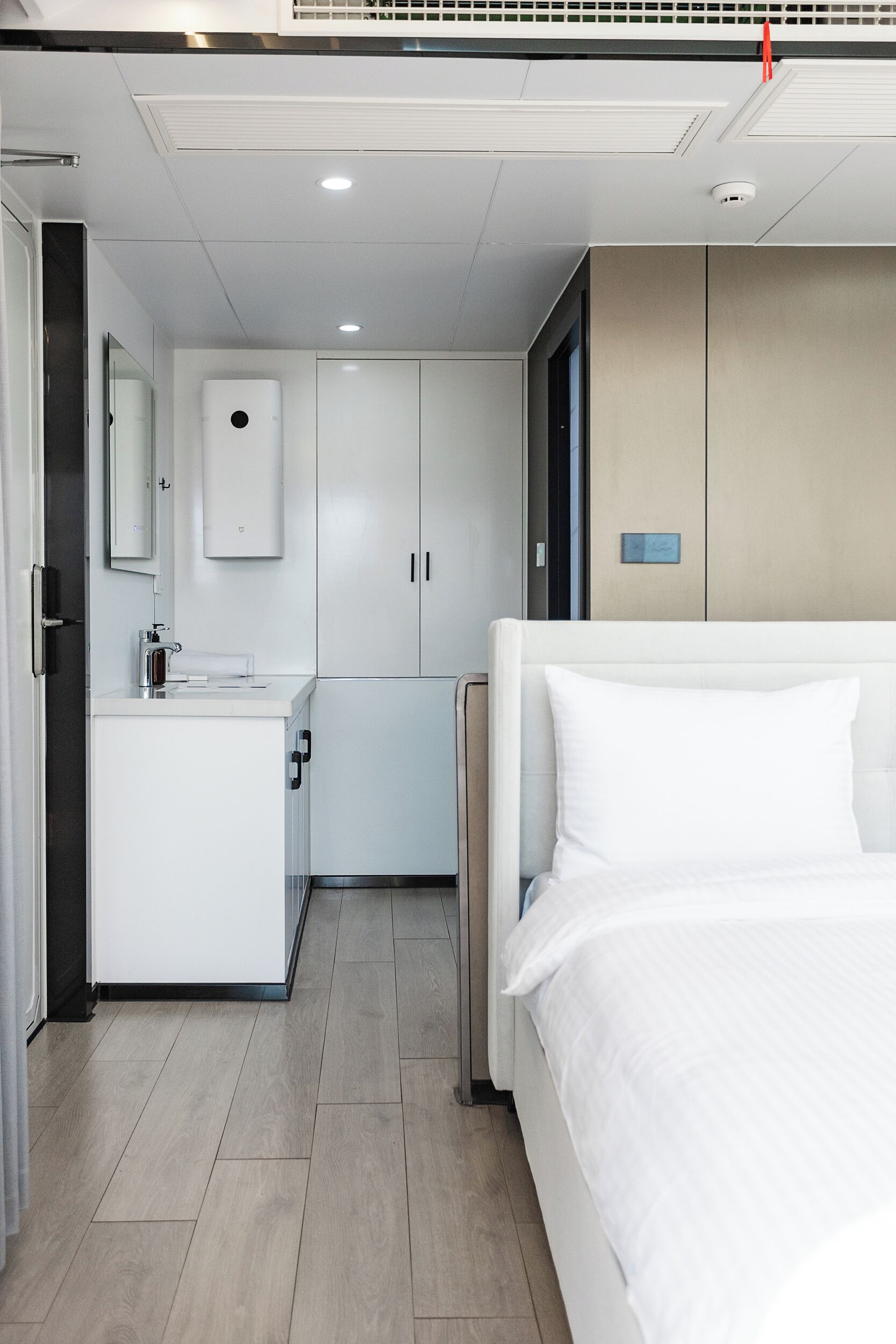 A modern hotel room with a bed, a small kitchenette, and a bathroom.