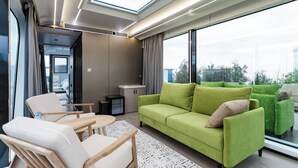 Et moderne interiør med en grøn sofa, en træstol, et lille bord og et stort vindue med udsigt til det fri.