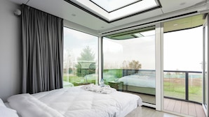 Et moderne soveværelse med en stor seng, et skydelugt og en skydedør til en balkon.
