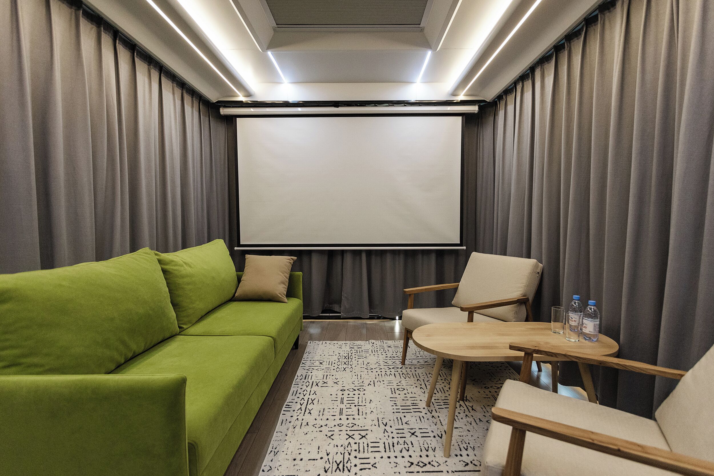 A room with a green sofa, a beige armchair, a wooden coffee table, and a projector screen.