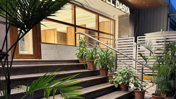 Entrada de un hotel con un letrero que dice "HOTEL DASYA", con un diseño moderno que incluye una escalera y plantas en macetas.