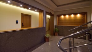Vestíbulo de hotel con mostrador de recepción, puertas de madera, una escalera y plantas en macetas.