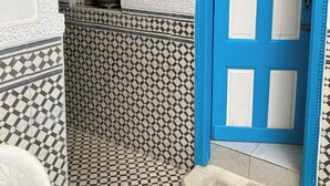 A blue door with white panels, a tiled floor with a geometric pattern, and a white chair. - 2 BEDROOM APARTMENT WITH SEAVIEW IN THE MEDINA (Essaouira)