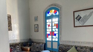 A cozy room with a patterned floor, a blue-framed window, a sofa with cushions, and a small round table. - 2 BEDROOM APARTMENT WITH SEAVIEW IN THE MEDINA (Essaouira)
