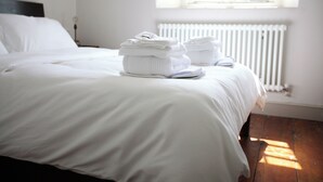A neatly made bed with white linens and towels stacked at the foot of the bed.