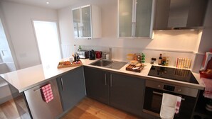 A modern kitchen with stainless steel appliances, a wooden floor, and white cabinetry.
