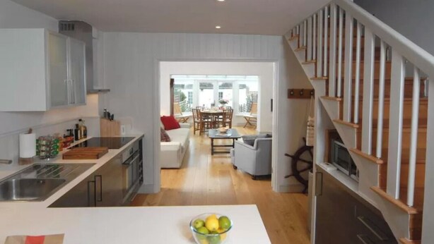 A modern kitchen with white cabinets, a central island with a bowl of fruit, and a dining area with a table and chairs.