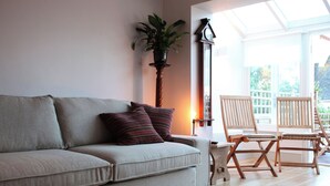 A living room with a beige sofa, striped pillows, a potted plant, and wooden chairs.