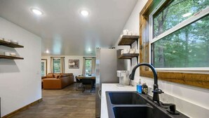 Eine moderne Küche mit zwei Spülen, Holzregalen und einem großen Fenster mit Blick auf einen Wald.