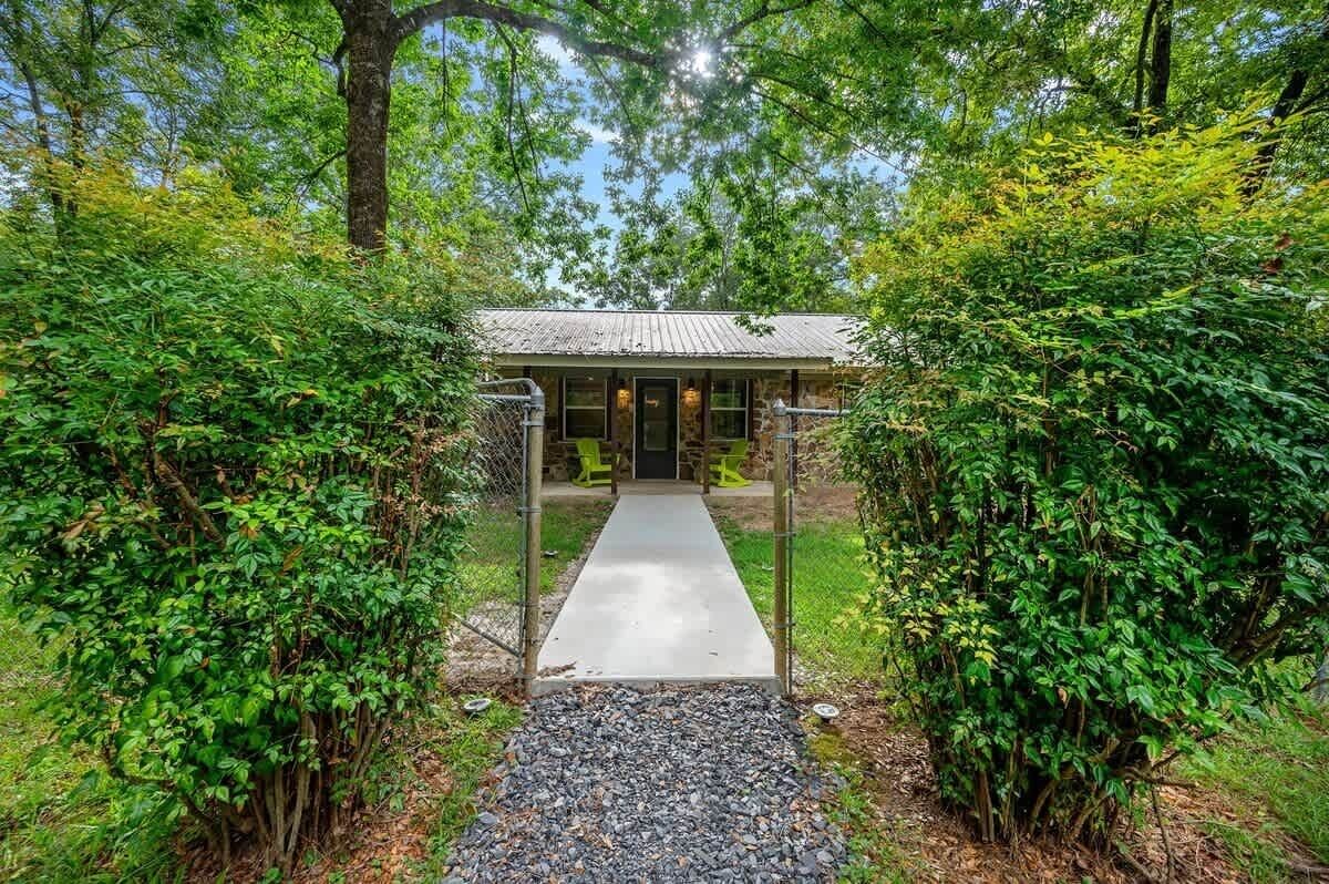 A rustic cabin with a concrete pathway leading to the entrance, surrounded by dense greenery.