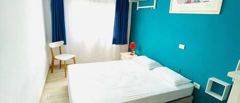 A bedroom with a bed, a chair, a nightstand, a lamp, and a framed picture on the wall.