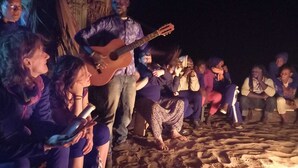 Een groep mensen staat 's nachts op het strand rond een gitarist.