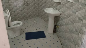 Een badkamer met betegelde vloer, een wit wastafelmeubel, een toilet en een douchehoek.