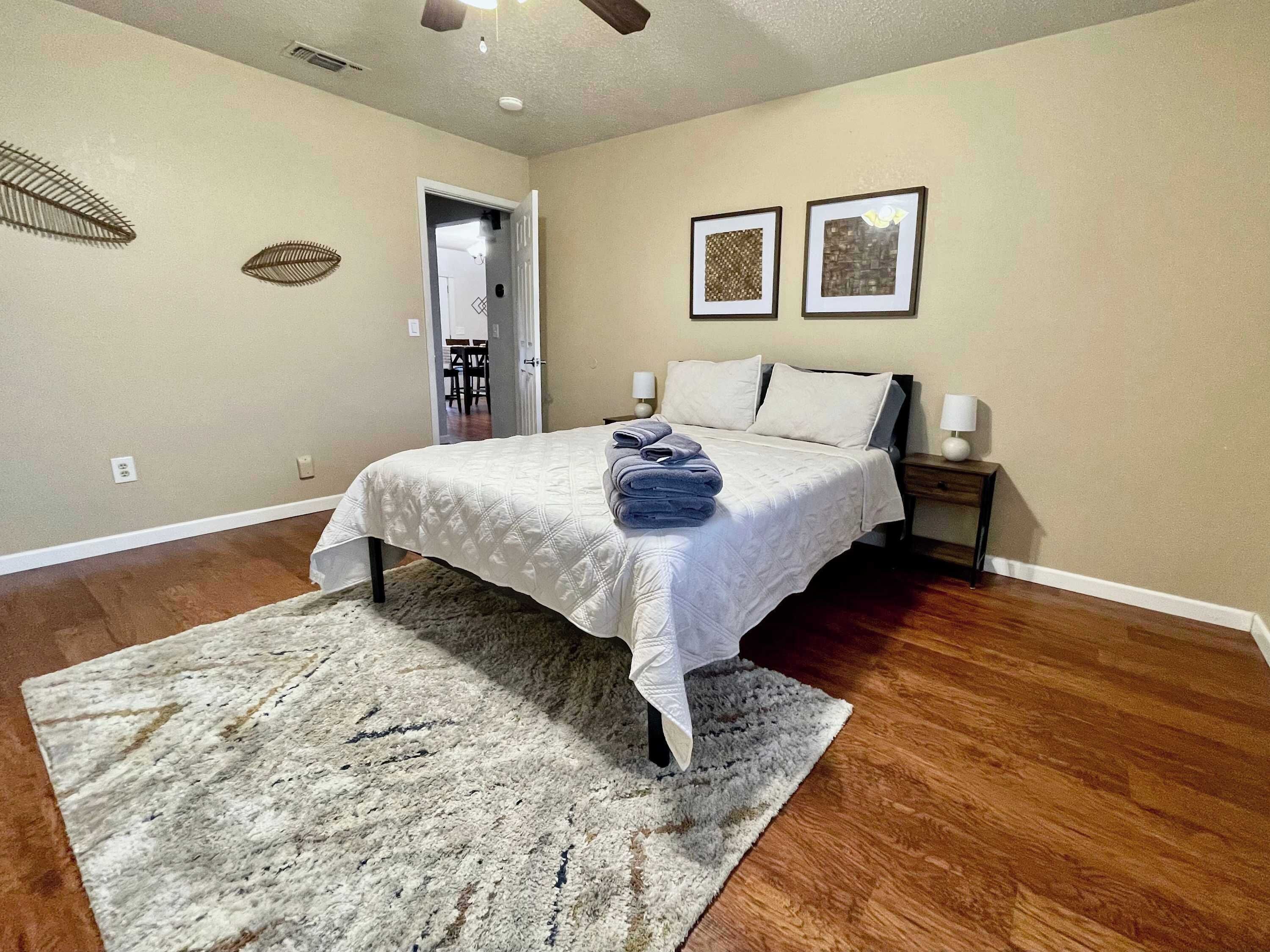 A bedroom with a bed, a rug, two wall art pieces, and a door leading to another room.