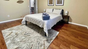 Quarto com cama, tapete, duas obras de arte nas paredes e porta para outro cômodo.