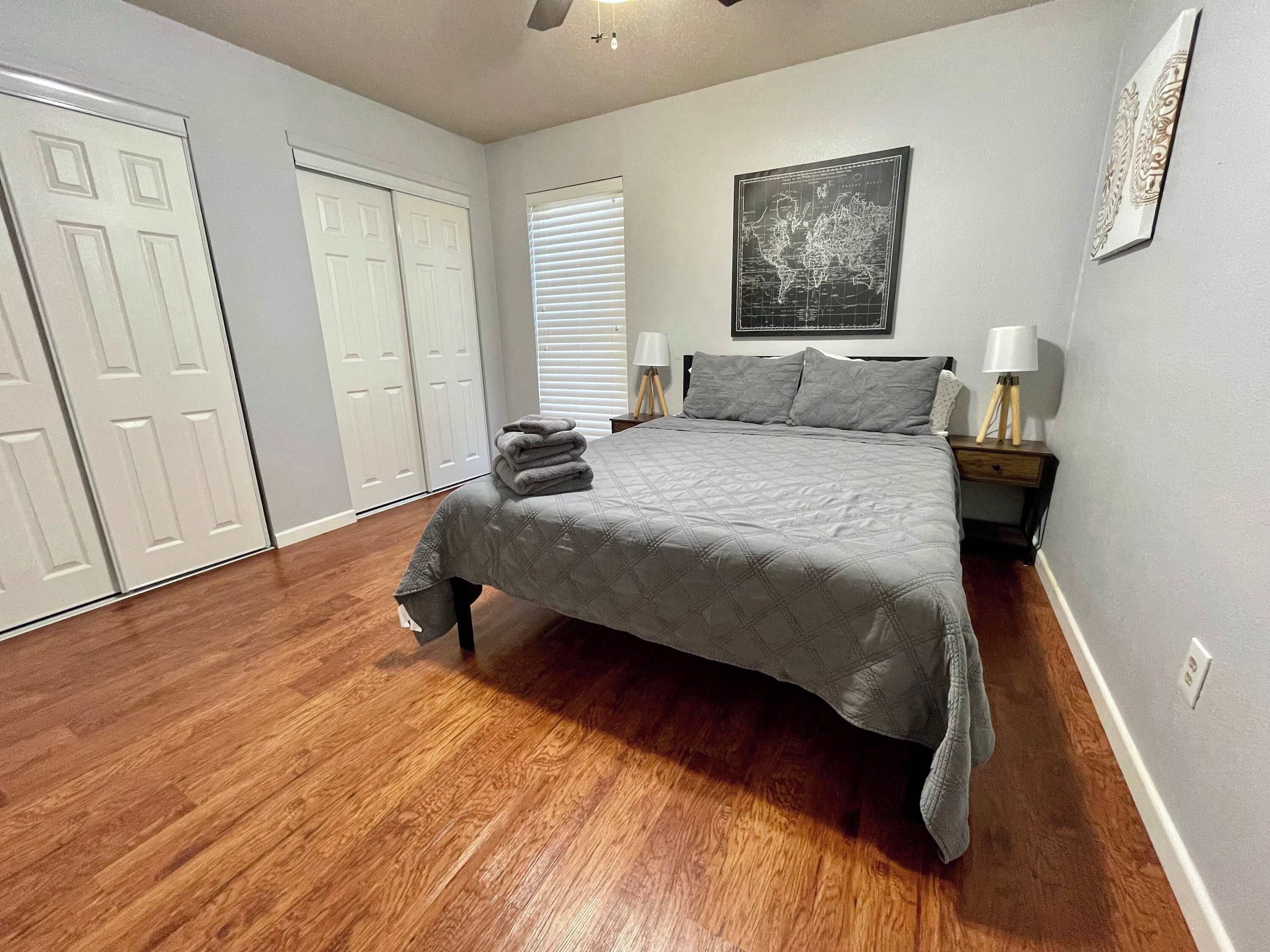 Une chambre à coucher avec un lit, deux tables de chevet avec des lampes, une carte accrochée au mur et une armoire avec des portes coulissantes.